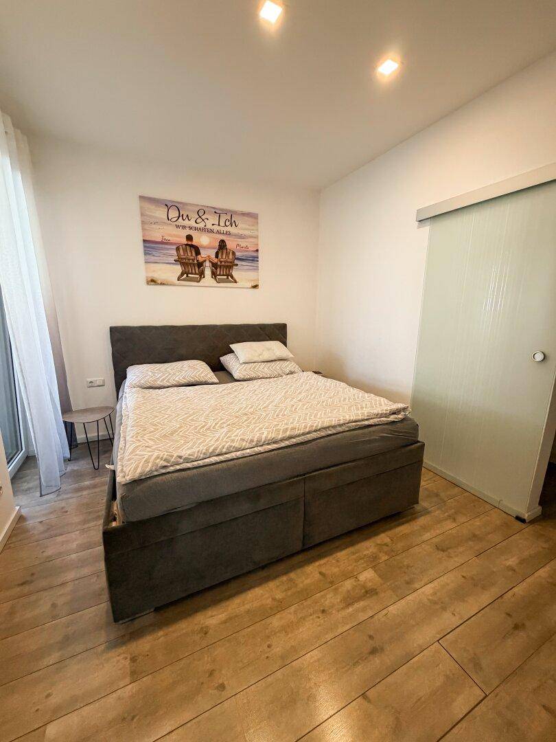 Gemütliches Schlafzimmer mit großem Bett, Laminatboden und viel natürlichem Licht.