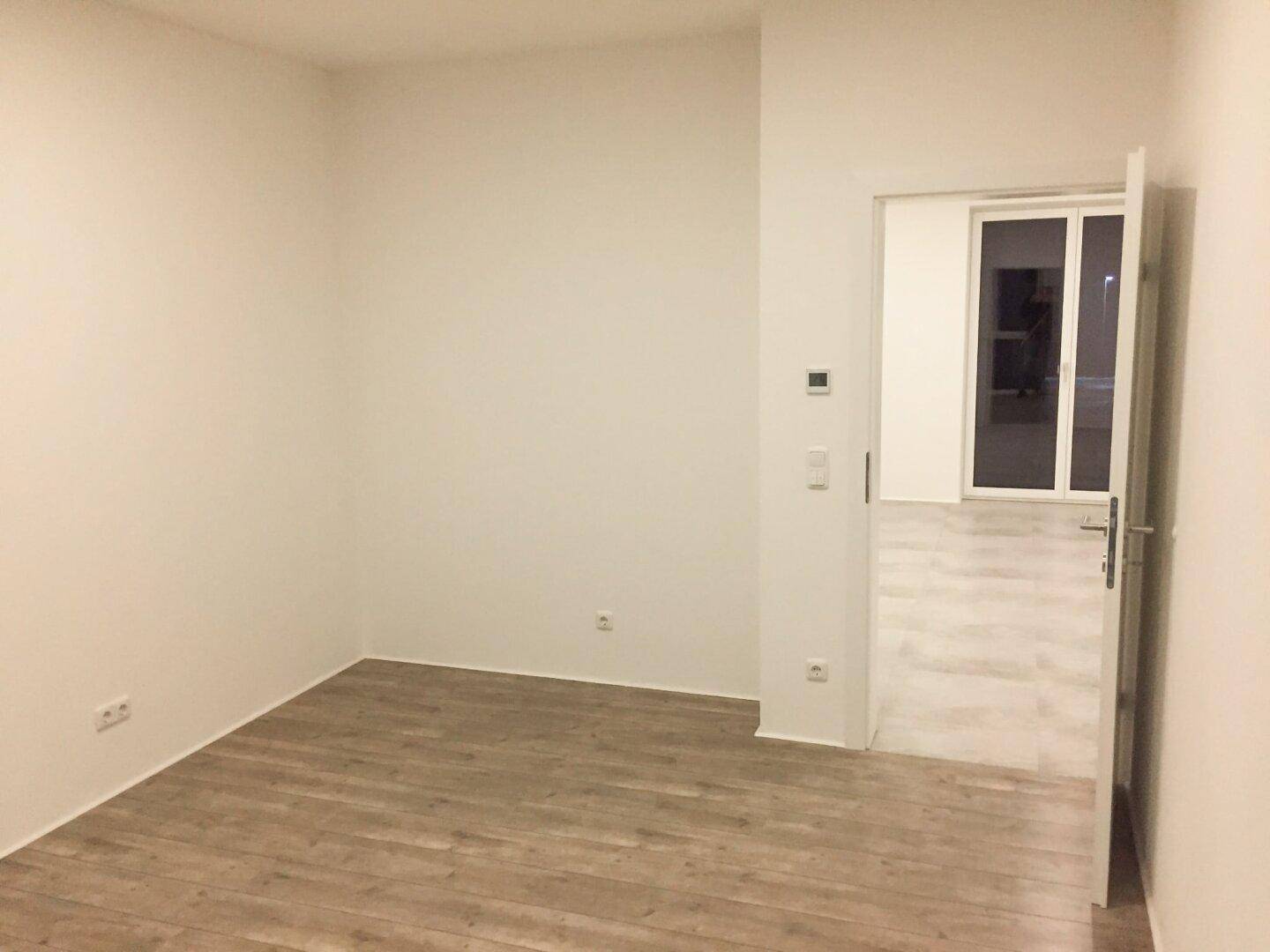 Leerer Raum mit Laminatboden und weiß gestrichenen Wänden, ideal für ein Schlafzimmer oder Büro.