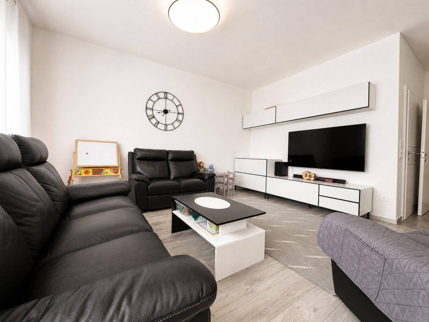 Geräumiges Wohnzimmer mit schwarzen Ledersofas, modernem TV-Möbel und hellem Laminatboden.