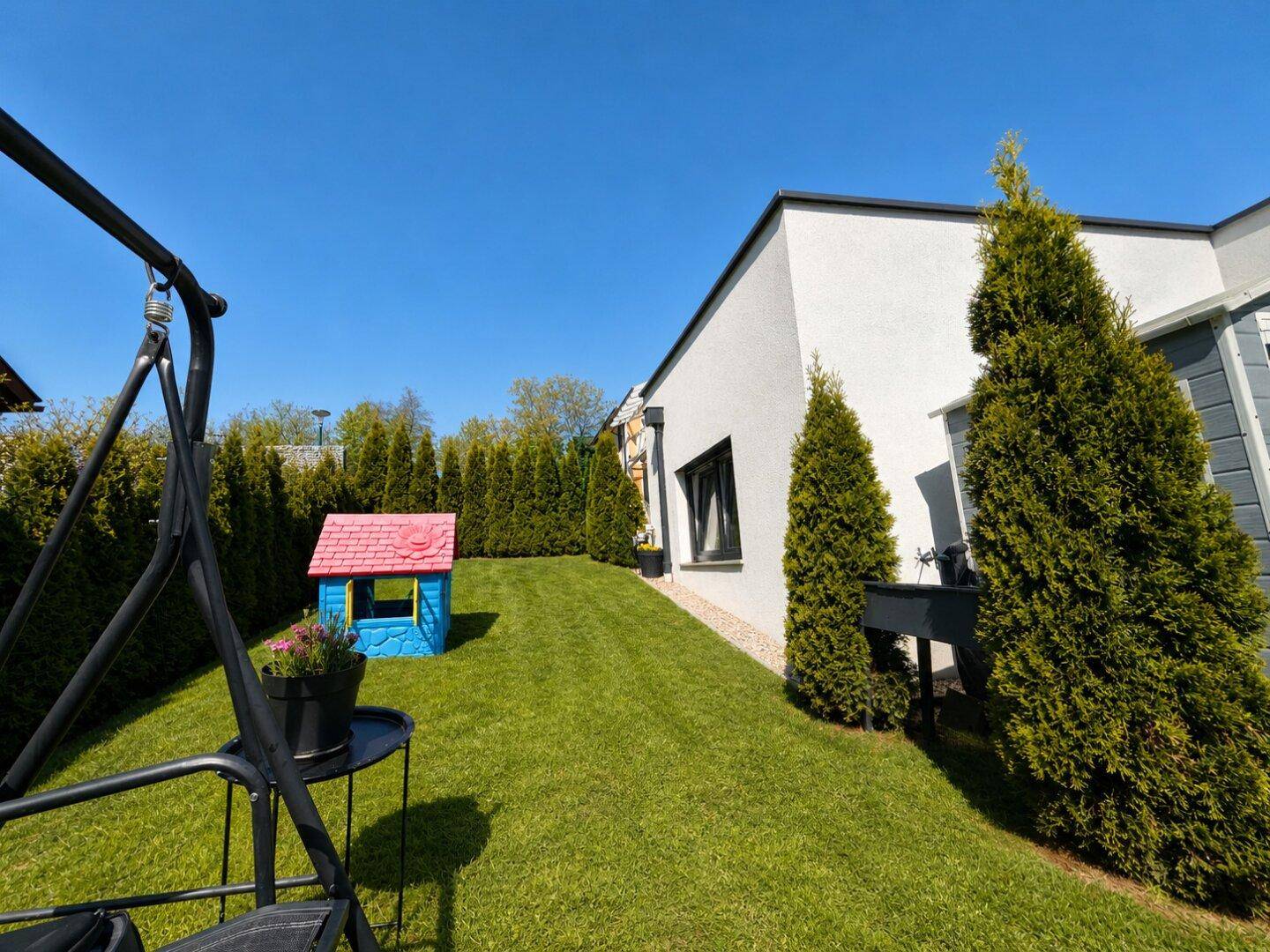Gepflegter Gartenbereich mit Rasenfläche, Kinderspielhaus und hohen Hecken für Privatsphäre.