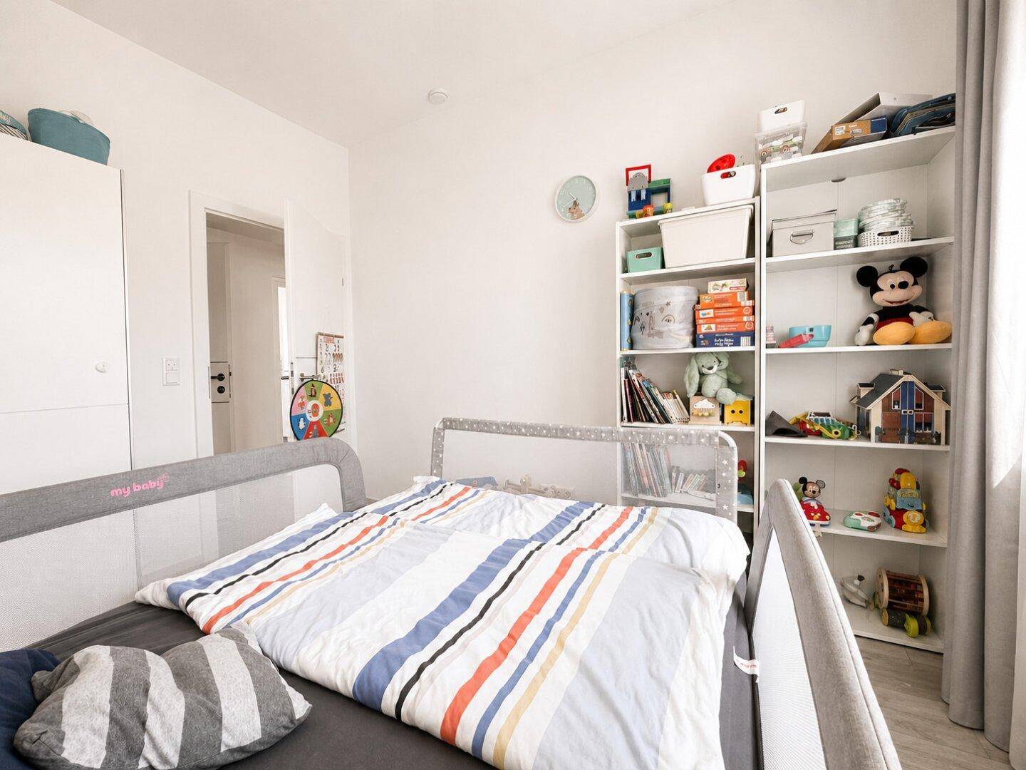 Helles Kinderzimmer mit Bett, weißem Regal und Spielzeug, das eine gemütliche Atmosphäre schafft.
