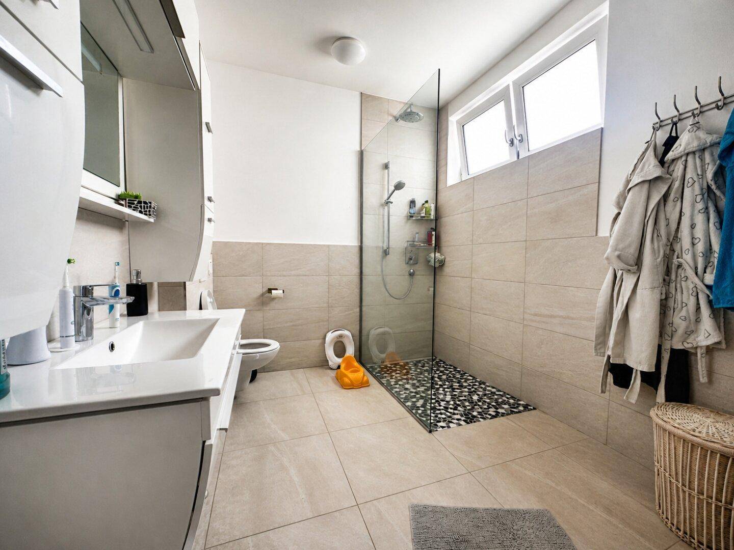 Modernes Badezimmer mit begehbarer Dusche, beigefarbenen Fliesen und Fenster für Tageslicht.