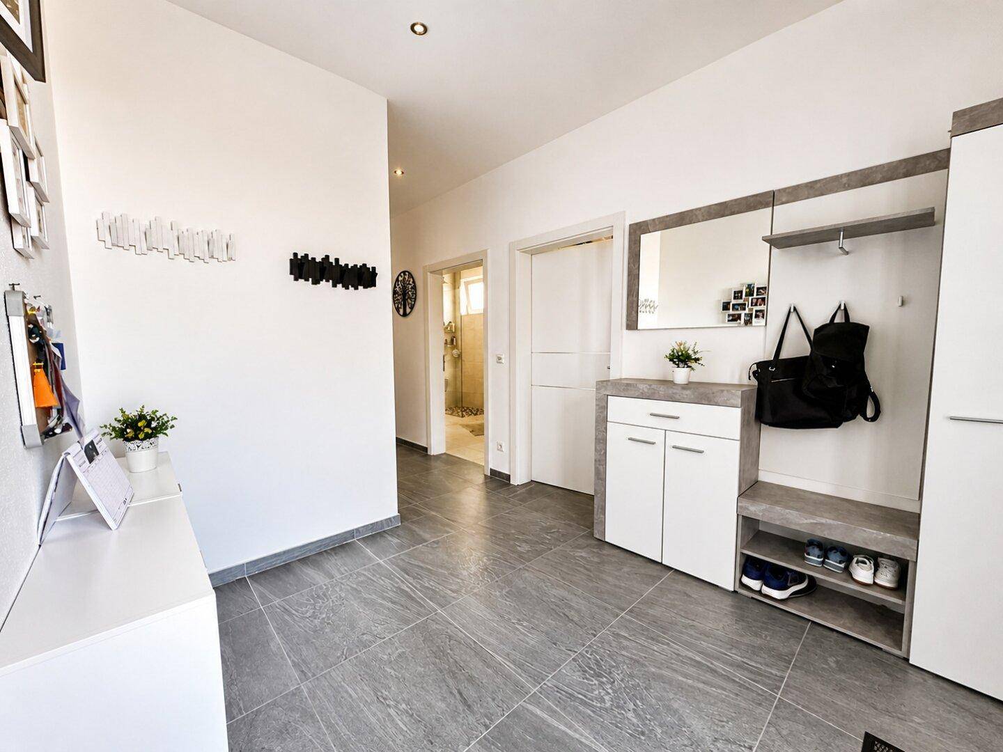 Geräumiger Eingangsbereich mit Garderobe, Spiegel und modernen grauen Bodenfliesen.