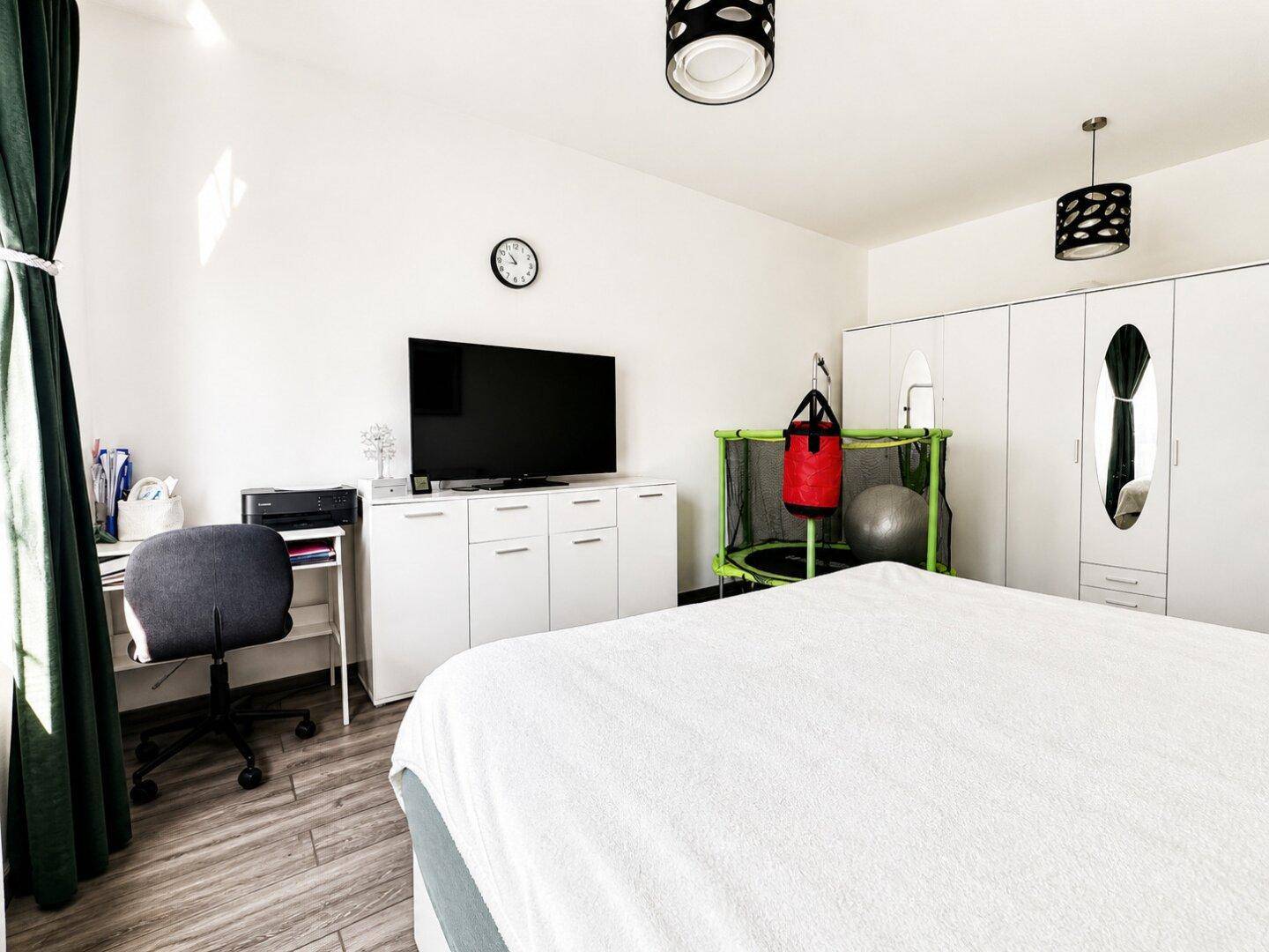 Schlafzimmer mit Doppelbett, Schreibtisch, Fernseher und großem Kleiderschrank mit Spiegeltür.