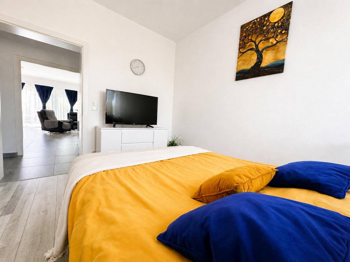 Helles Schlafzimmer mit Doppelbett und Blick in den angrenzenden Wohnbereich.