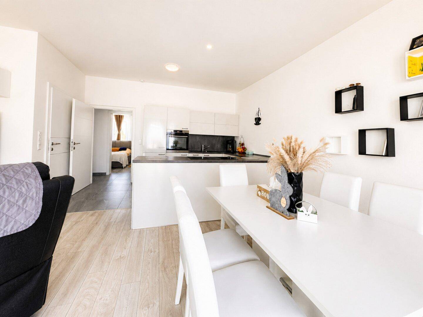 Moderne offene Küche mit weißen Schränken, Essbereich und direktem Zugang zum Wohnzimmer.