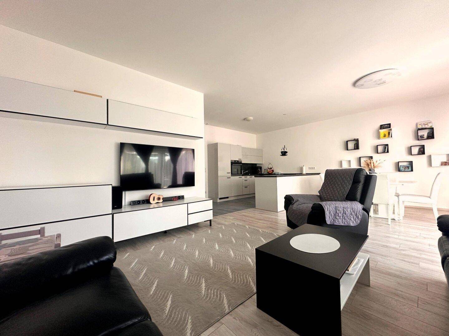 Geräumiger offener Wohnbereich mit TV-Möbel, Sofa und Blick auf die moderne Küche.