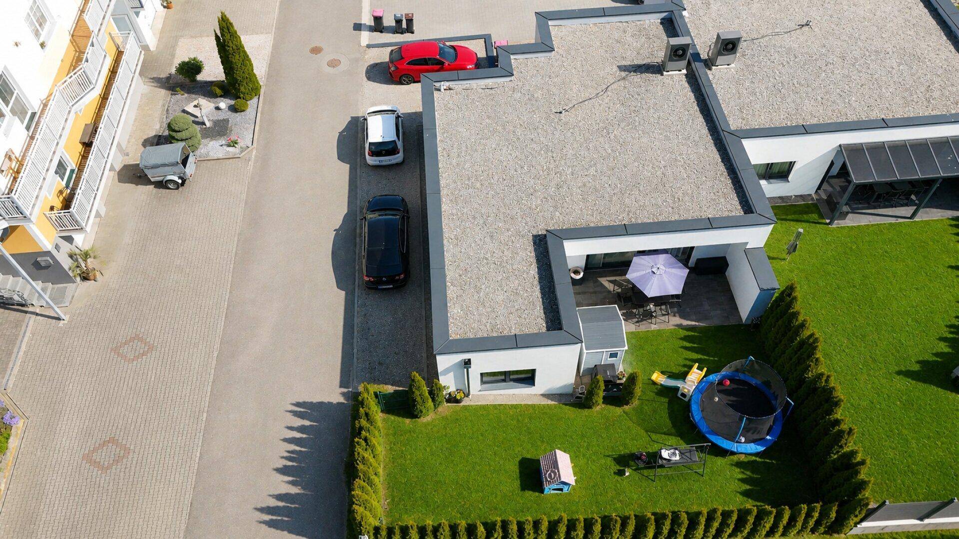 Luftaufnahme des modernen Einfamilienhauses mit Flachdach, Garten und gepflasterter Zufahrt.