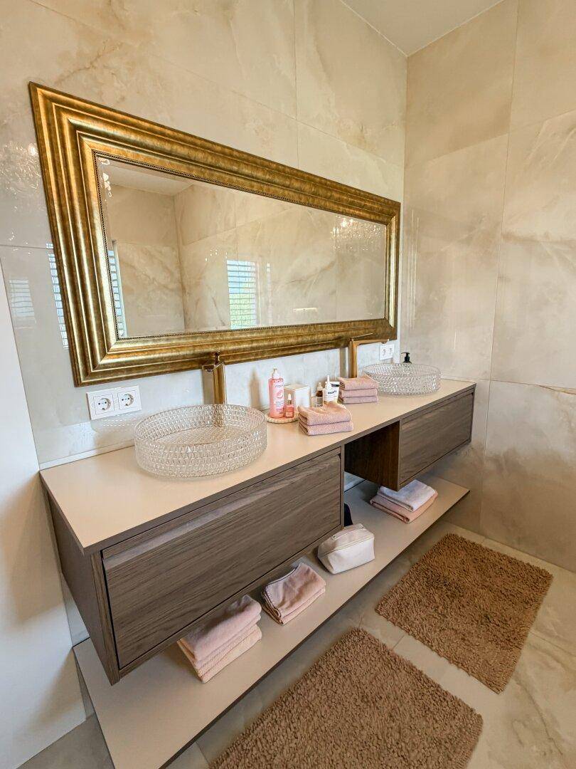 Modernes Badezimmer mit Doppelwaschbecken, großem vergoldeten Spiegel und Marmorfliesen.