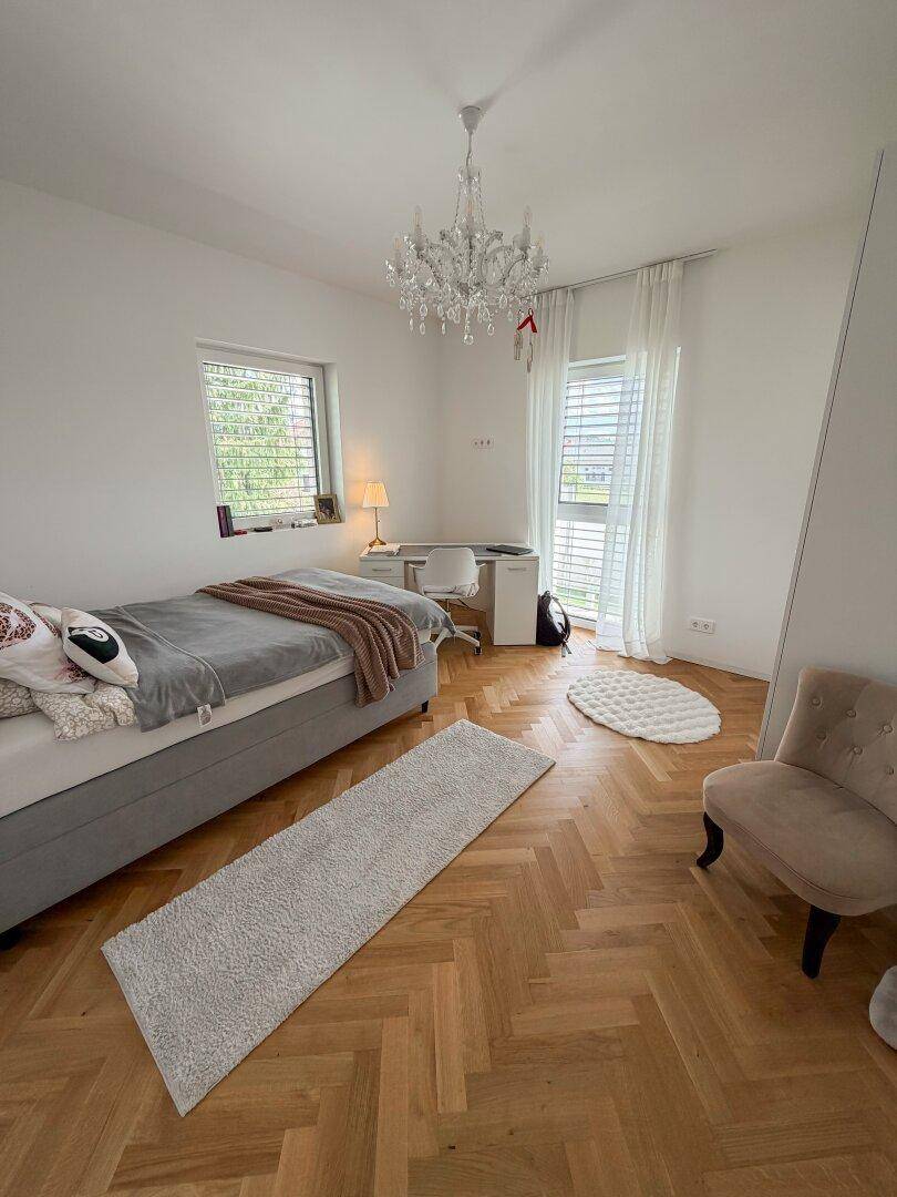 Kinderzimmer mit Einzelbett, Schreibtisch und großen Fenstern, die viel Tageslicht hereinlassen.