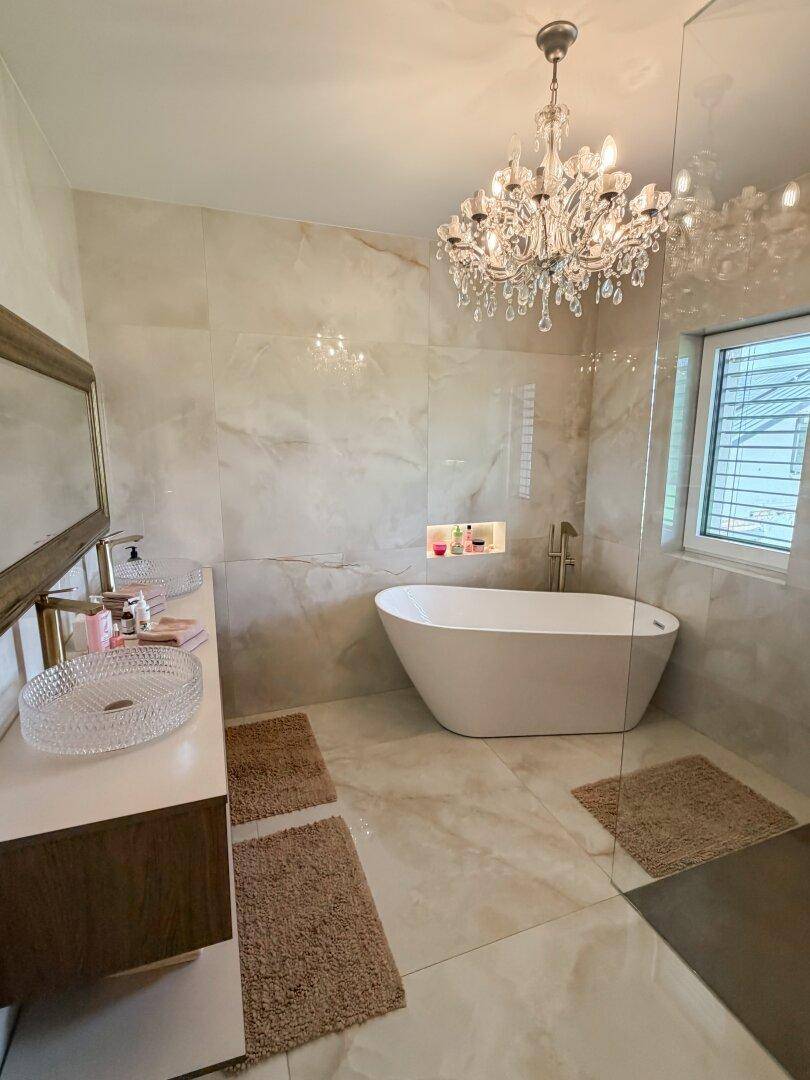 Luxuriöses Badezimmer mit freistehender Badewanne, Dusche und funkelndem Kronleuchter.