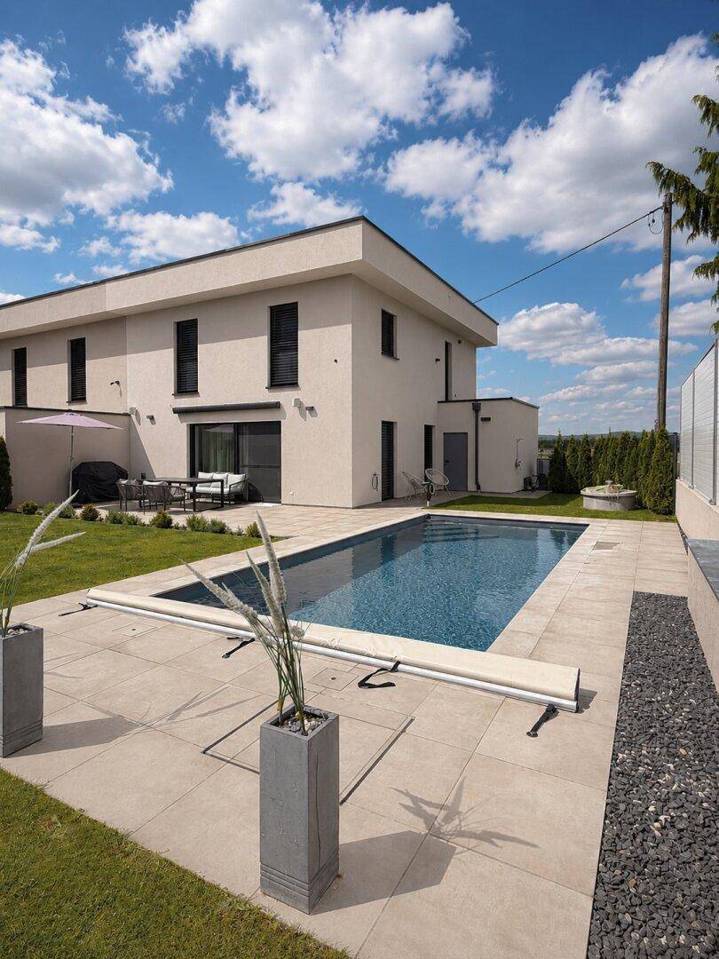 Rückansicht des modernen Hauses mit großem Pool und weitläufigem Garten unter blauem Himmel.