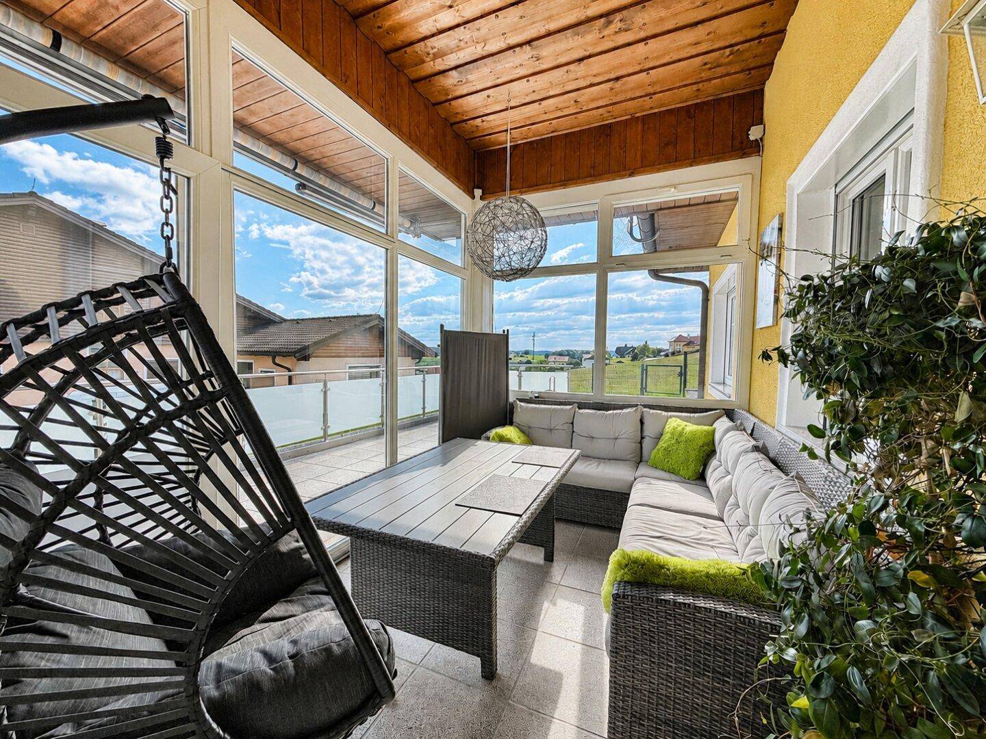 Gemütlicher Wintergarten mit Rattanmöbeln, Holzdach und weitem Blick in die Landschaft.