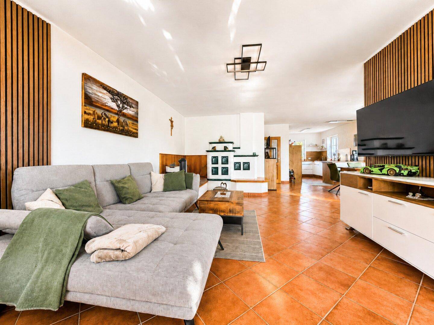 Geräumiges Wohnzimmer mit Terrakotta-Fliesenboden, modernem Sofa und Kachelofen im Hintergrund.