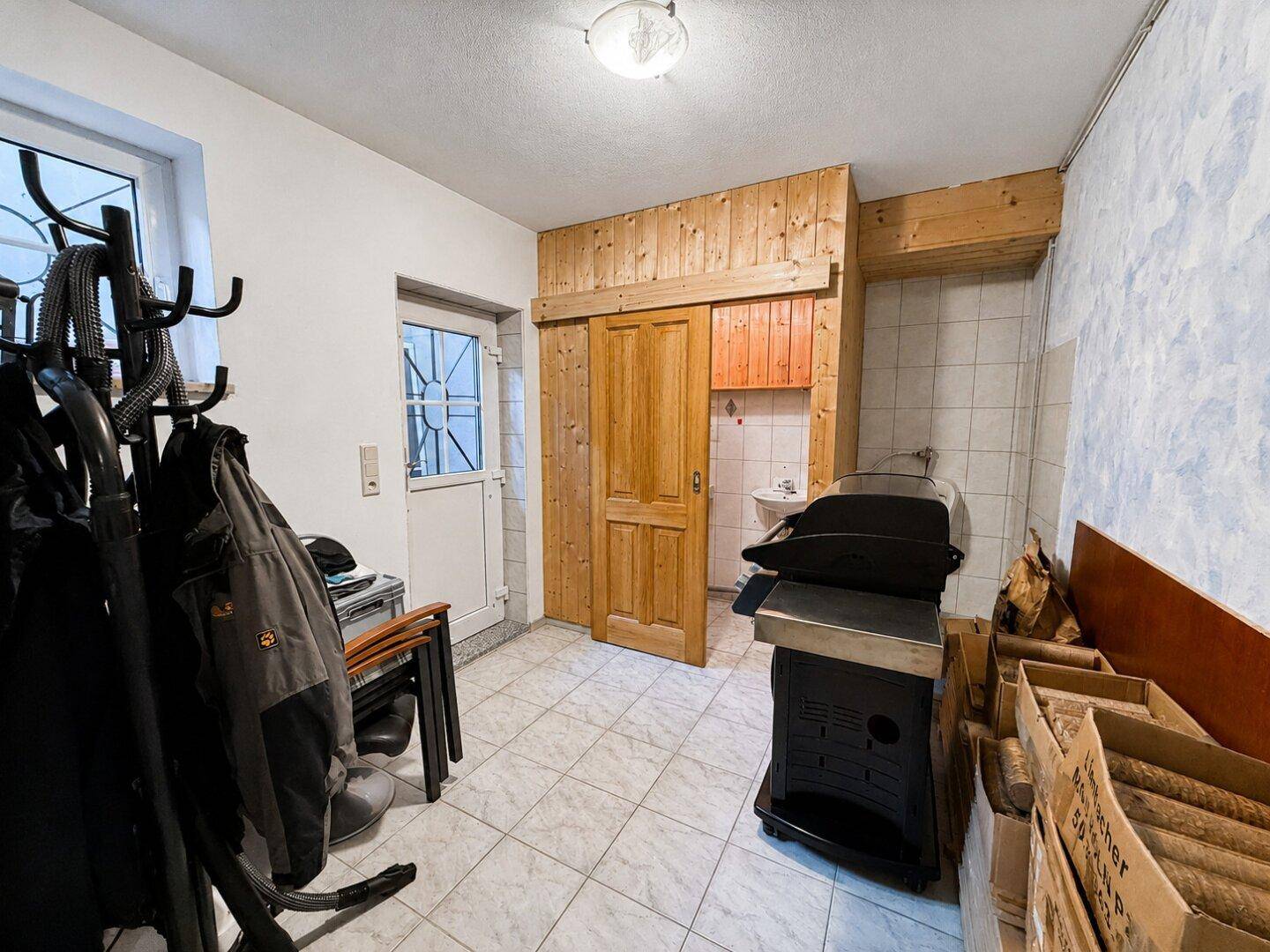 Eingangsbereich mit Fliesenboden, Garderobe und einem Grill, der auf den Außenbereich hindeutet.
