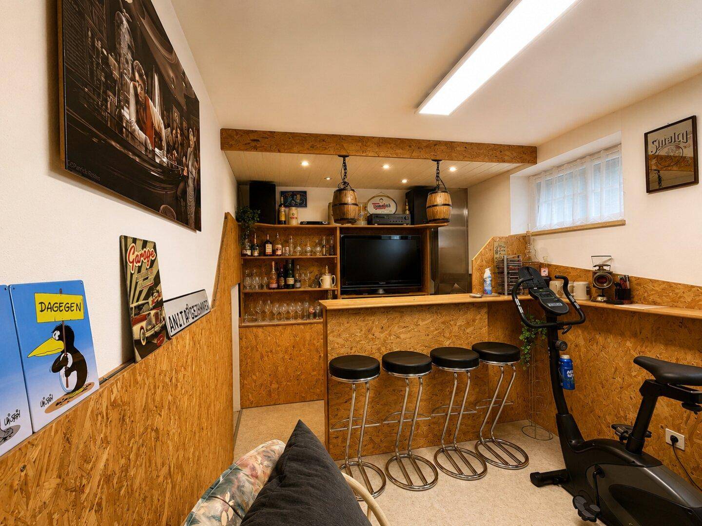 Ausgebauter Kellerraum mit Bar, Hockern und einem Fitnessgerät, ideal für Freizeitaktivitäten.