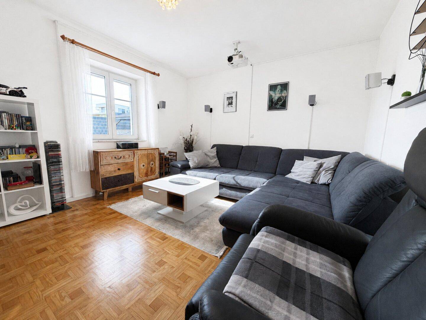 Helles Wohnzimmer mit Parkettboden, großem Sofa und Projektor für Heimkinoabende.
