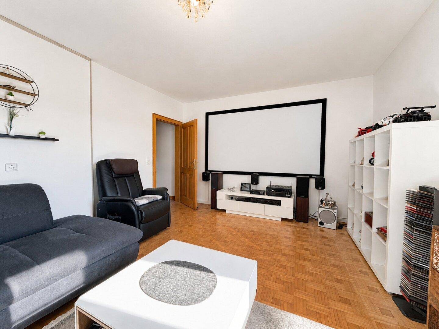 Geräumiges Wohnzimmer mit großem Projektionsbildschirm und Parkettboden für Unterhaltung.