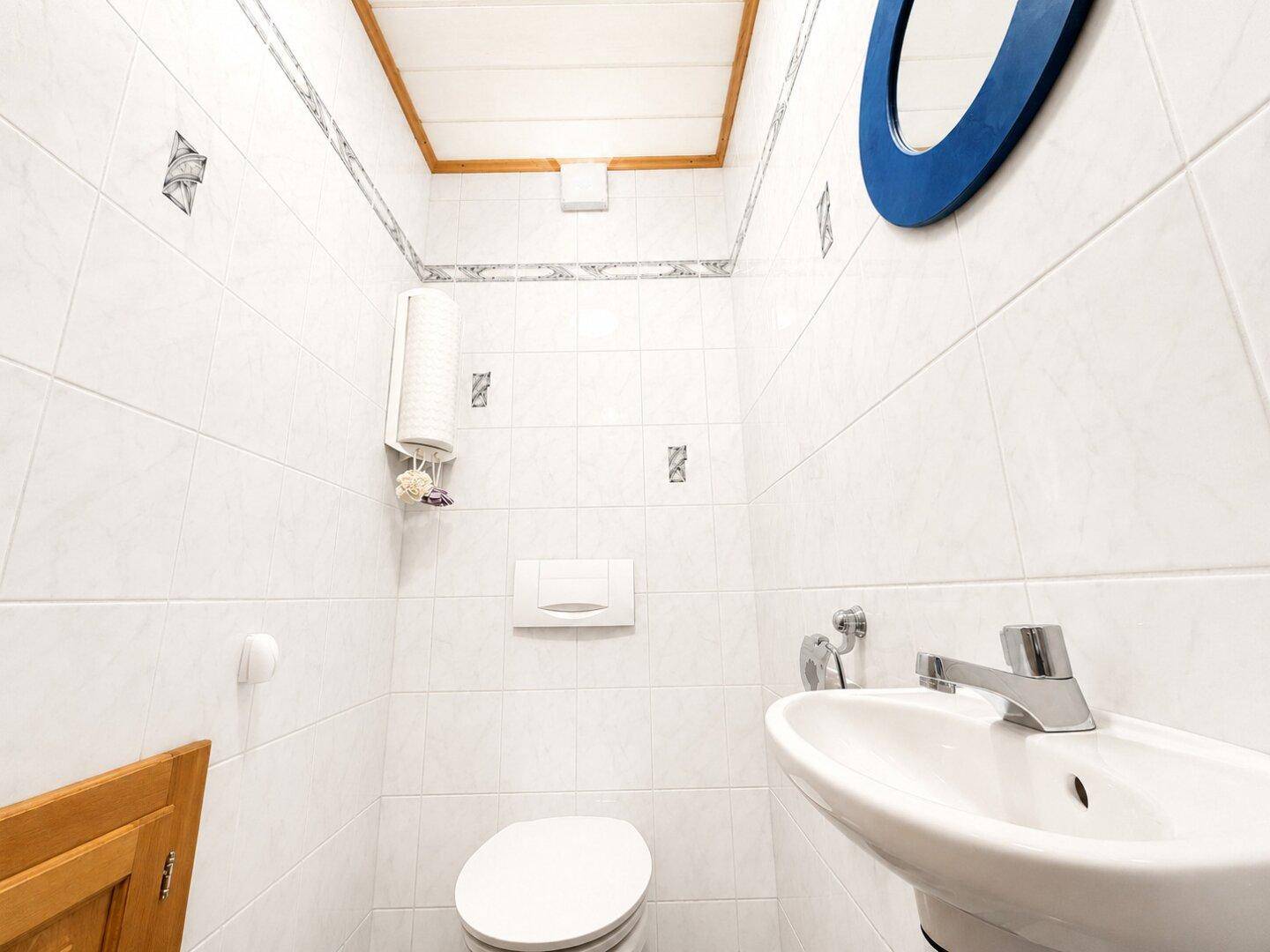 Kleines Gäste-WC mit weißen Fliesen, Toilette und einem einzelnen Waschbecken.