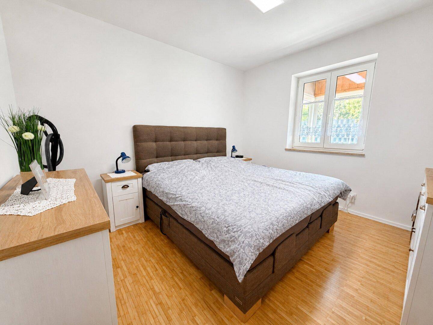 Helles Schlafzimmer mit Doppelbett, Holzmöbeln und Fenster für natürliches Licht.