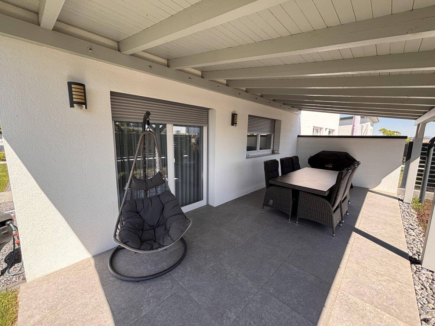 Überdachte Terrasse mit modernen Outdoor-Möbeln, Hängesessel und großformatigen Fliesen.