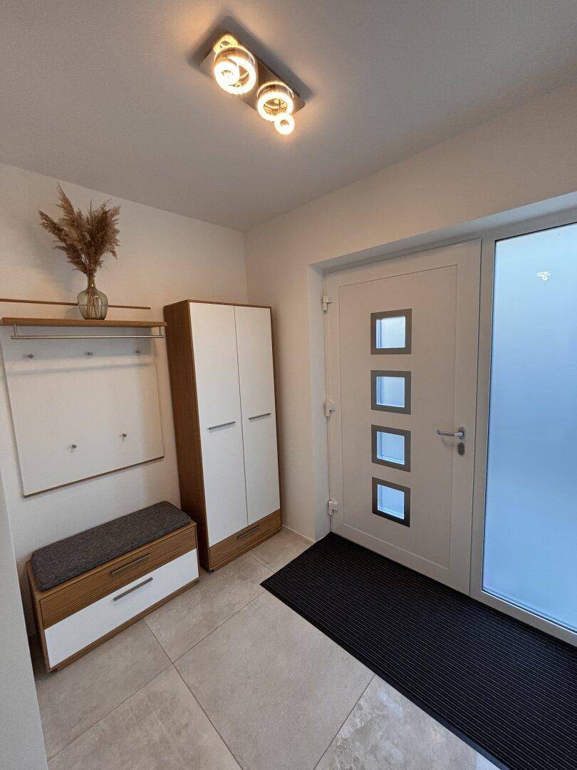 Heller Eingangsbereich mit moderner weißer Tür, Schuhschrank und Garderobe.