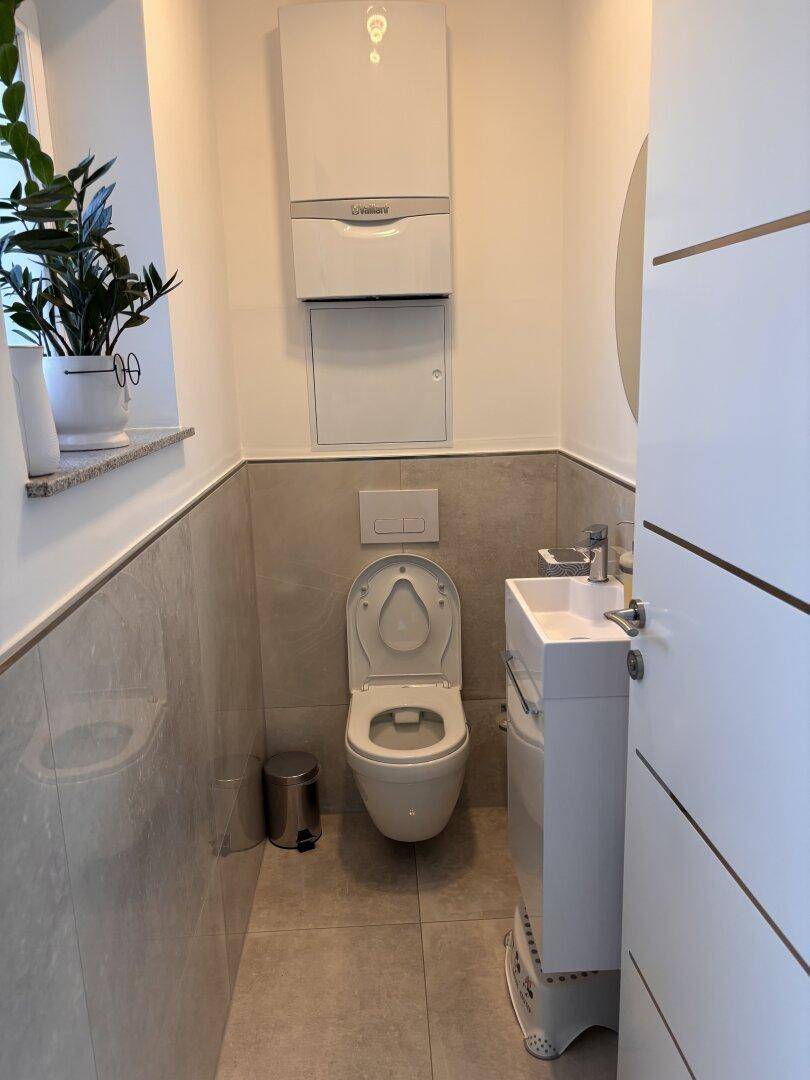 Modernes Gäste-WC mit wandhängender Toilette, kleinem Waschbecken und Fenster.