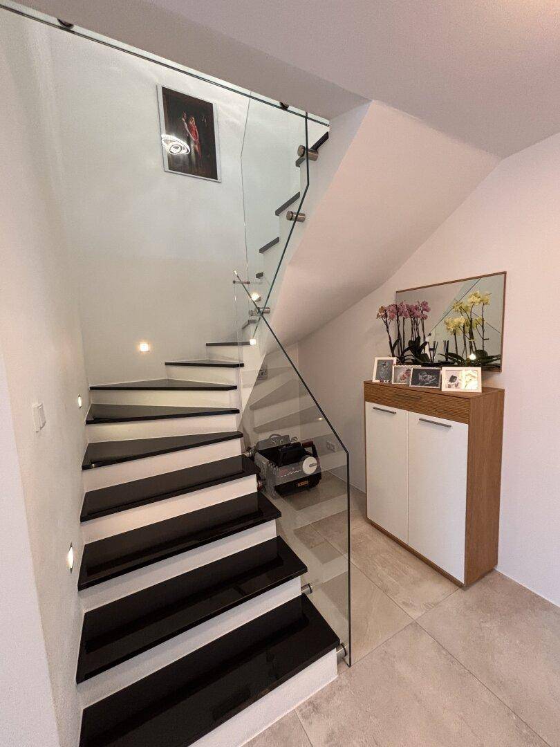 Elegante moderne Treppe mit schwarzen Stufen, Glasgeländer und indirekter Beleuchtung.