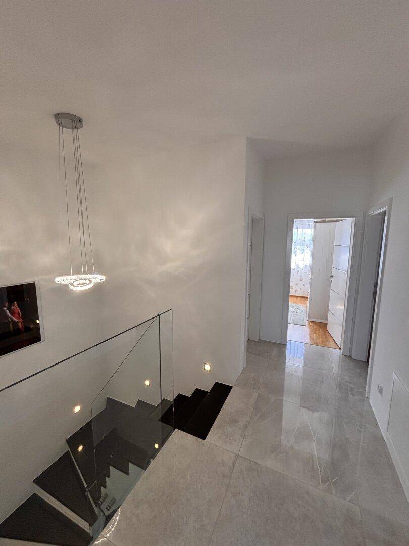 Heller Flur im Obergeschoss mit moderner Treppe, glänzenden Fliesen und Zugang zu weiteren Räumen.