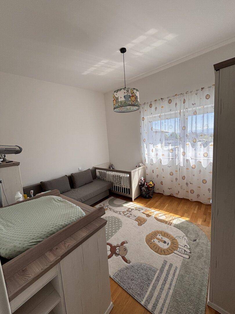 Helles Kinderzimmer mit Babybett, Wickeltisch, Sofa und warmem Holzfußboden.