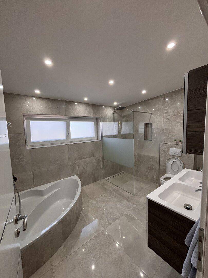 Modernes Badezimmer mit Badewanne, begehbarer Dusche, Doppelwaschbecken und großformatigen Fliesen.