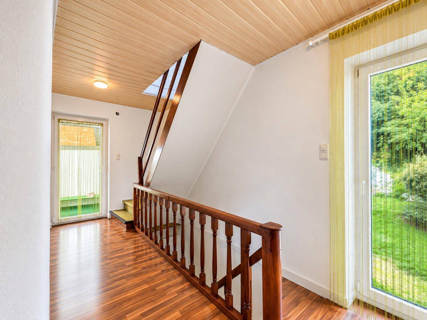 Heller Flur mit Holzvertäfelung an der Decke und Holztreppe zum Obergeschoss.