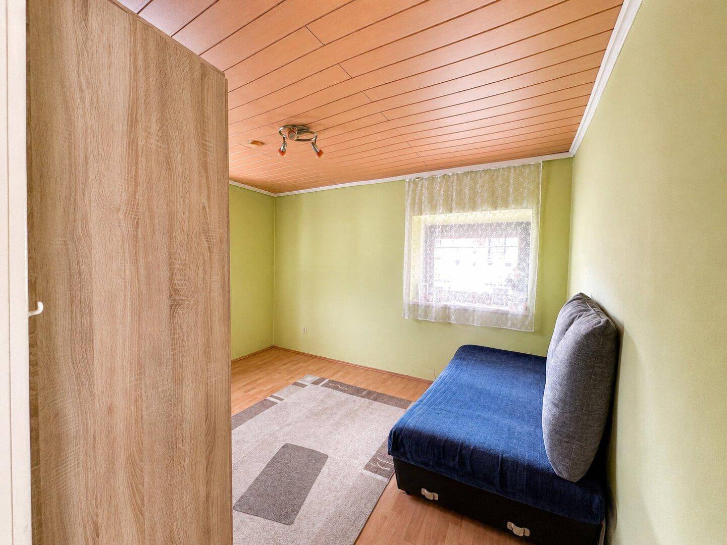 Schlafzimmer mit hellgrünen Wänden, Holzdecke und einem Einzelbett.