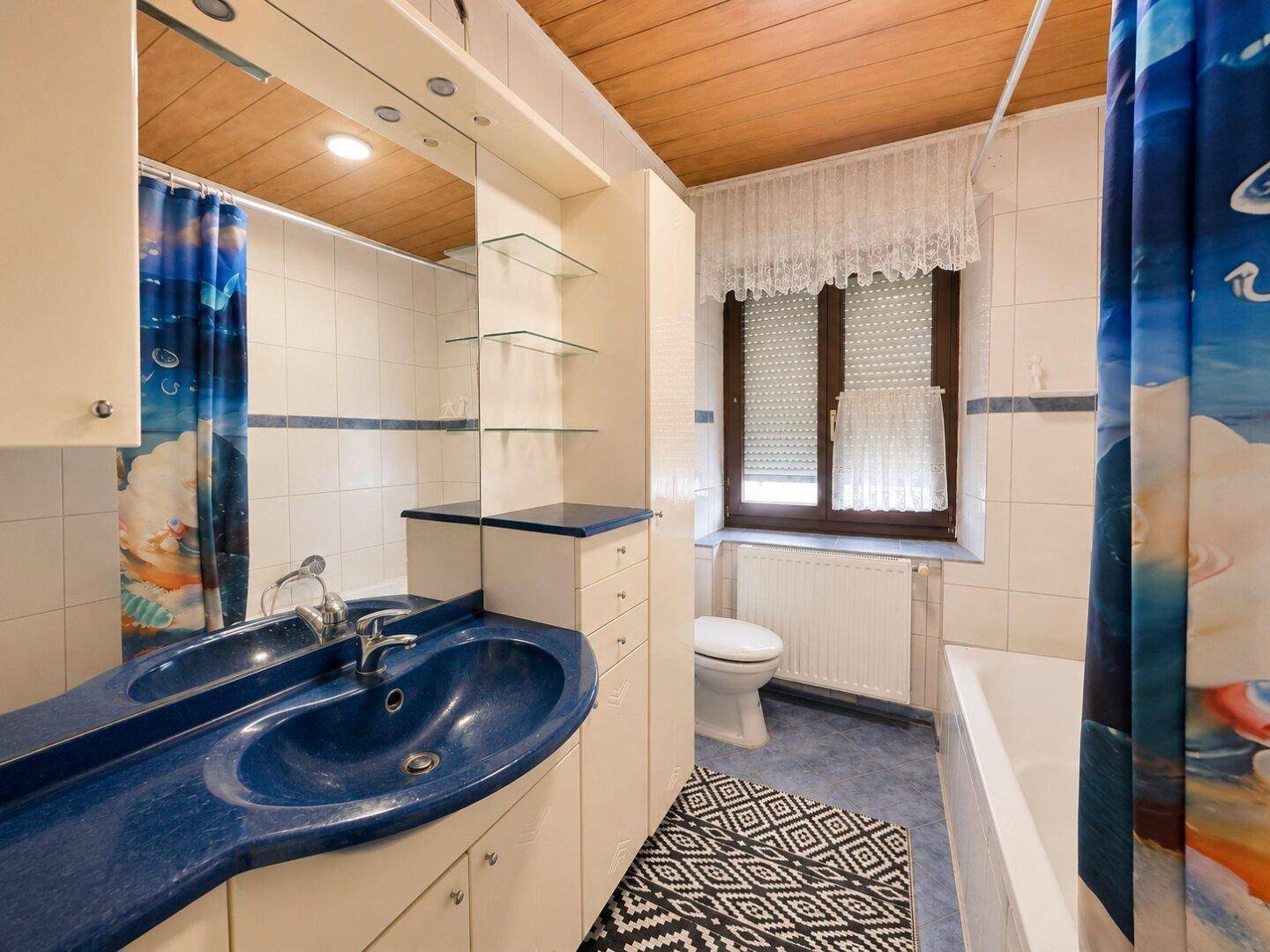 Badezimmer mit blauen und weißen Fliesen, Holzdecke und einem blauen Waschbecken.