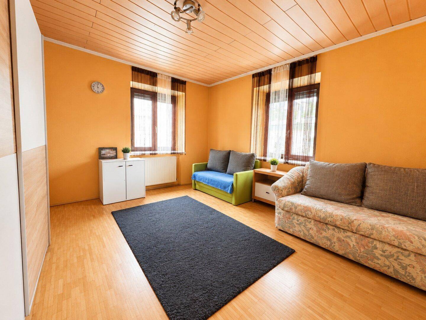 Geräumiges Wohnzimmer mit orangefarbenen Wänden, Holzdecke und zwei Sofas.