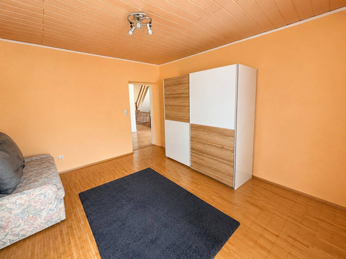 Schlafzimmer mit orangefarbenen Wänden, Holzdecke und einem Kleiderschrank.