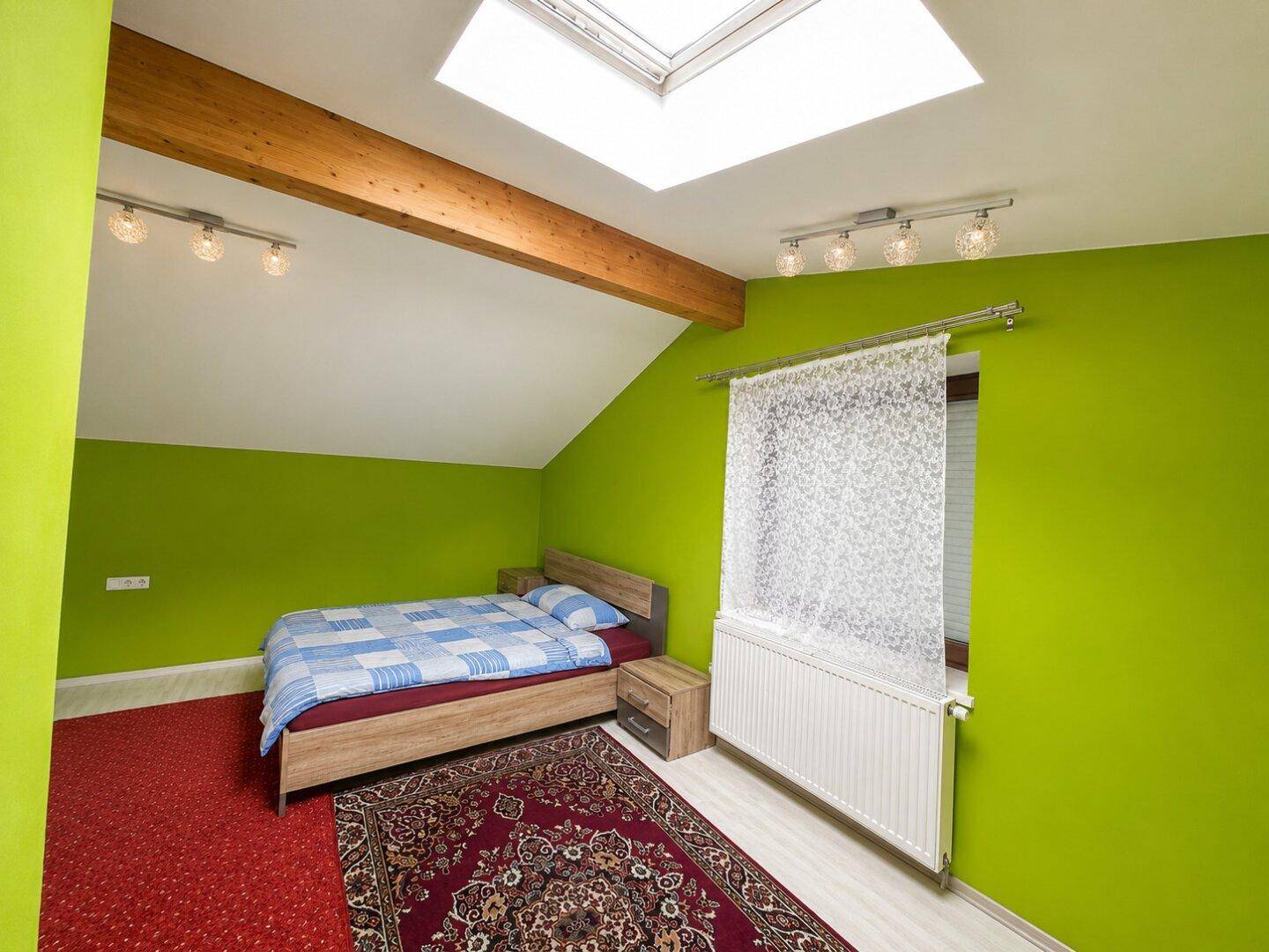Dachschlafzimmer mit schrägen Wänden, grün gestrichen und einem Doppelbett unter dem Dachfenster.