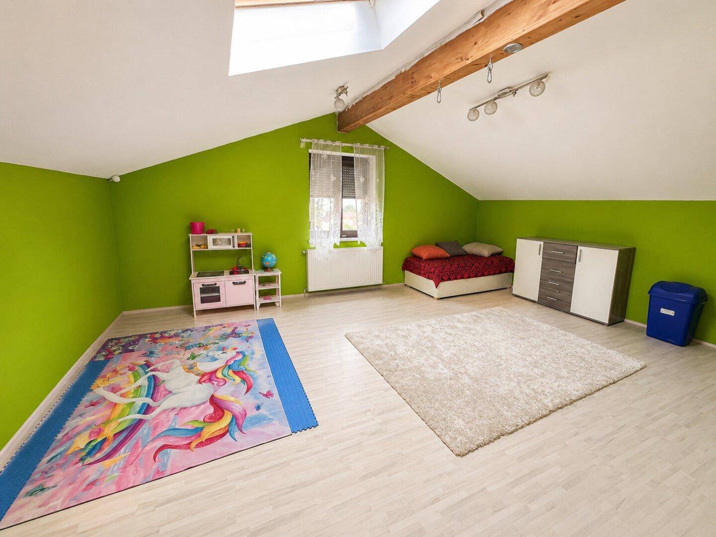 Geräumiges Dachzimmer mit grünen Wänden, Dachfenster und Spielbereich.