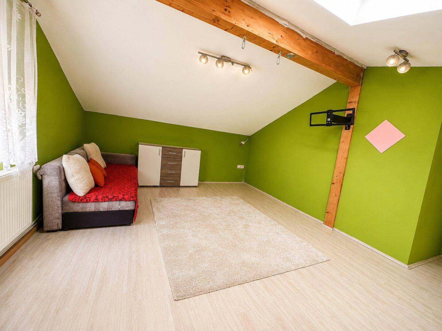 Dachwohnzimmer mit grünen Wänden, schrägen Decken und einem Sofa.