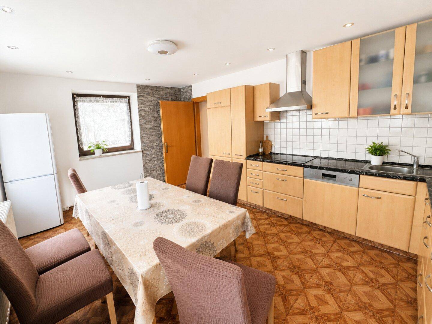 Helle Küche mit Holzfronten, Esstisch und Kühlschrank.