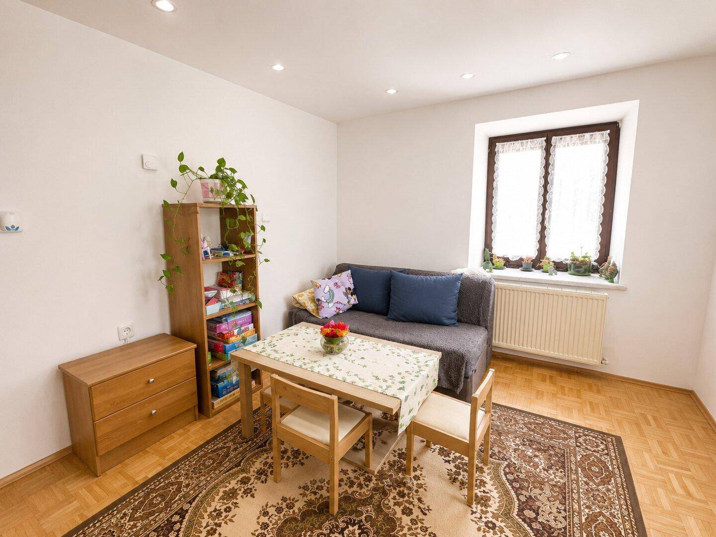 Kleines Wohnzimmer mit Sofa, Esstisch und Teppichboden.