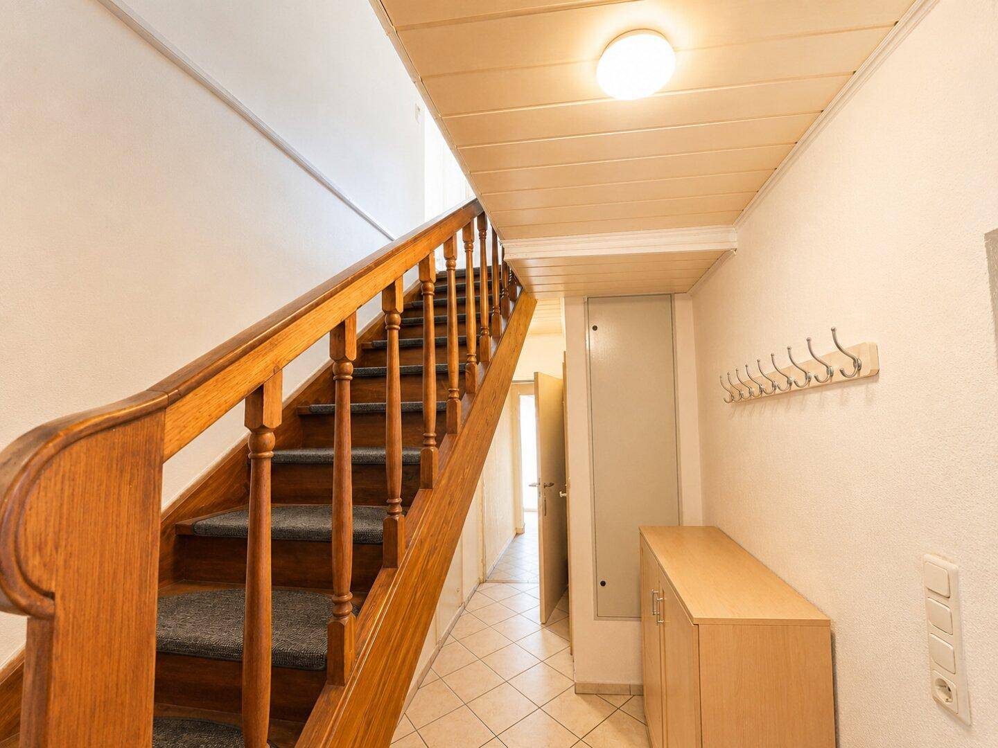 Flur mit Holztreppe, Garderobe und Fliesenboden.