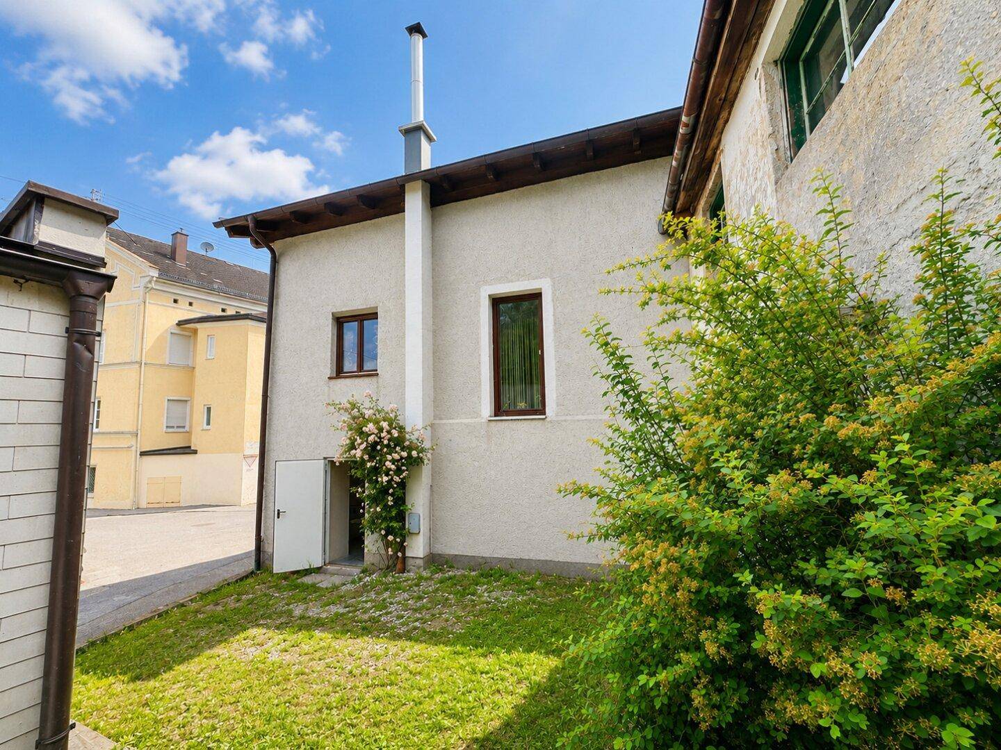 Seitenansicht eines Hauses mit Gartenbereich und grüner Bepflanzung.