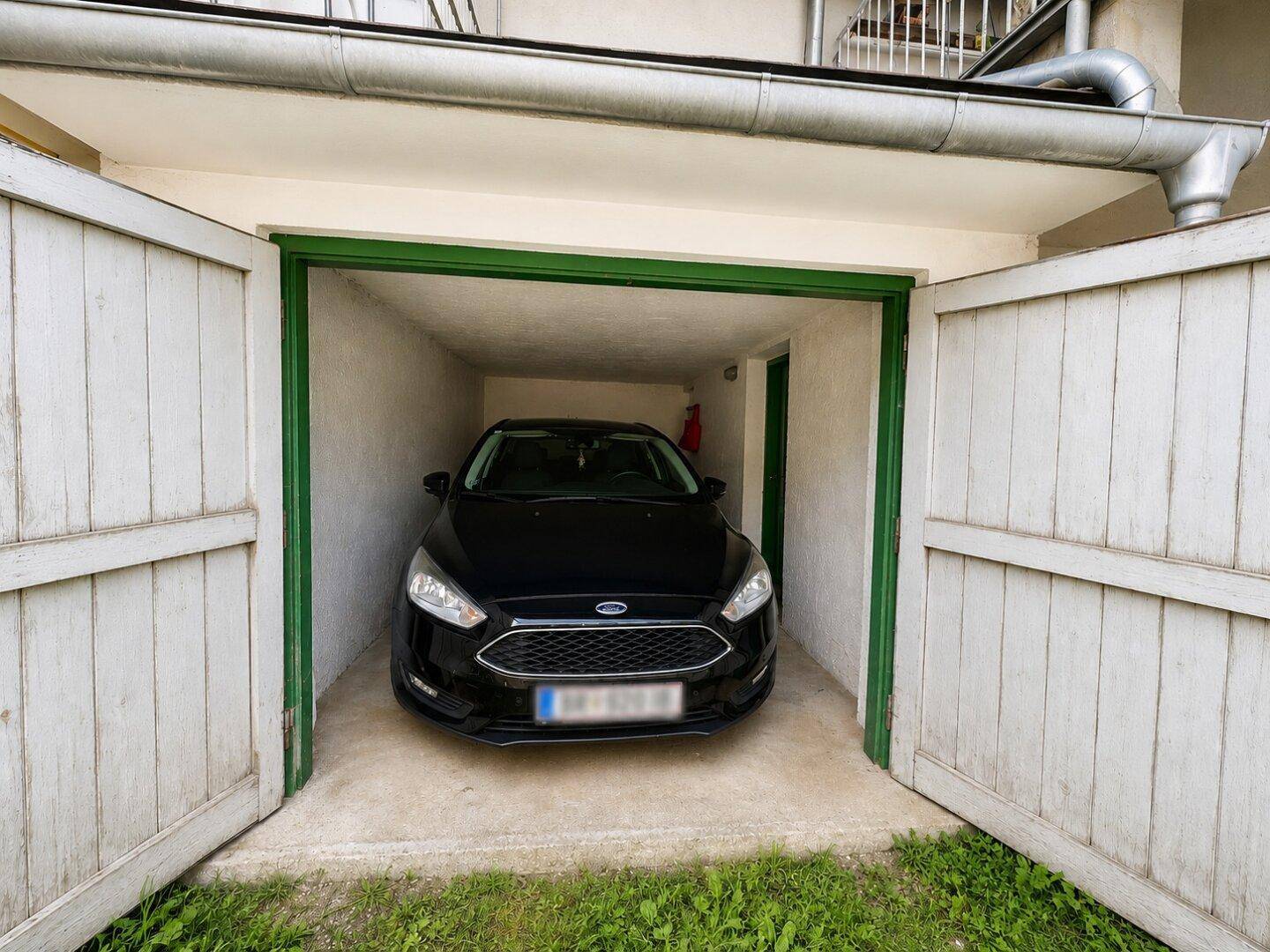 Schwarzes Auto in einer Garage mit geöffneten Holztüren und einer Regenrinne darüber.