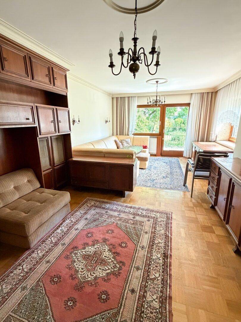 Gemütliches Wohnzimmer mit traditionellen Holzmöbeln, Parkettboden und Zugang zu einem Balkon.