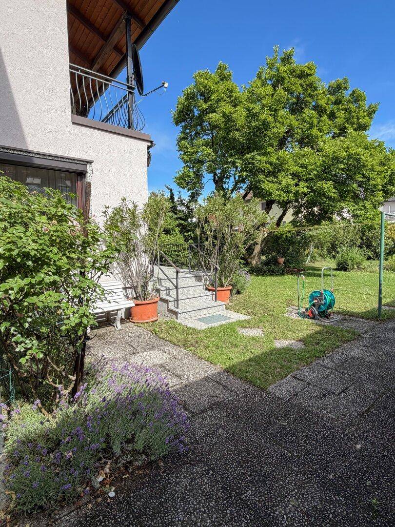 Gepflegter Gartenbereich mit Rasenfläche, gepflastertem Weg und Treppe zum Haus.