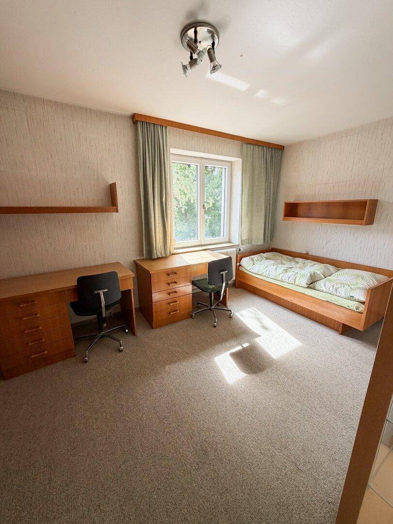 Helles Schlafzimmer mit Teppichboden, Einzelbett und zwei Schreibtischen, ideal als Kinder- oder Arbeitszimmer.