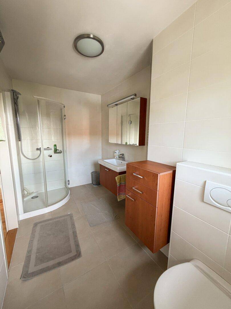 Modernisiertes Badezimmer mit hellen Fliesen, Duschkabine und wandhängendem WC für zeitgemäßen Komfort.