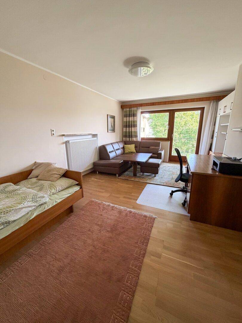 Heller Raum mit Parkettboden, Sofa, Einzelbett und Schreibtischbereich, ideal für Gäste oder als Arbeitszimmer.