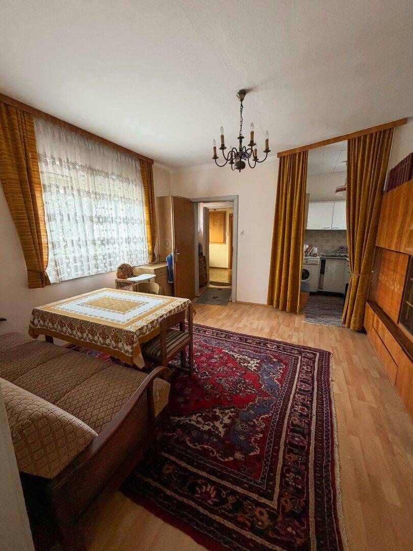 Wohnzimmer mit Holzboden, Sofa und Blick auf eine kleine Küchenzeile.